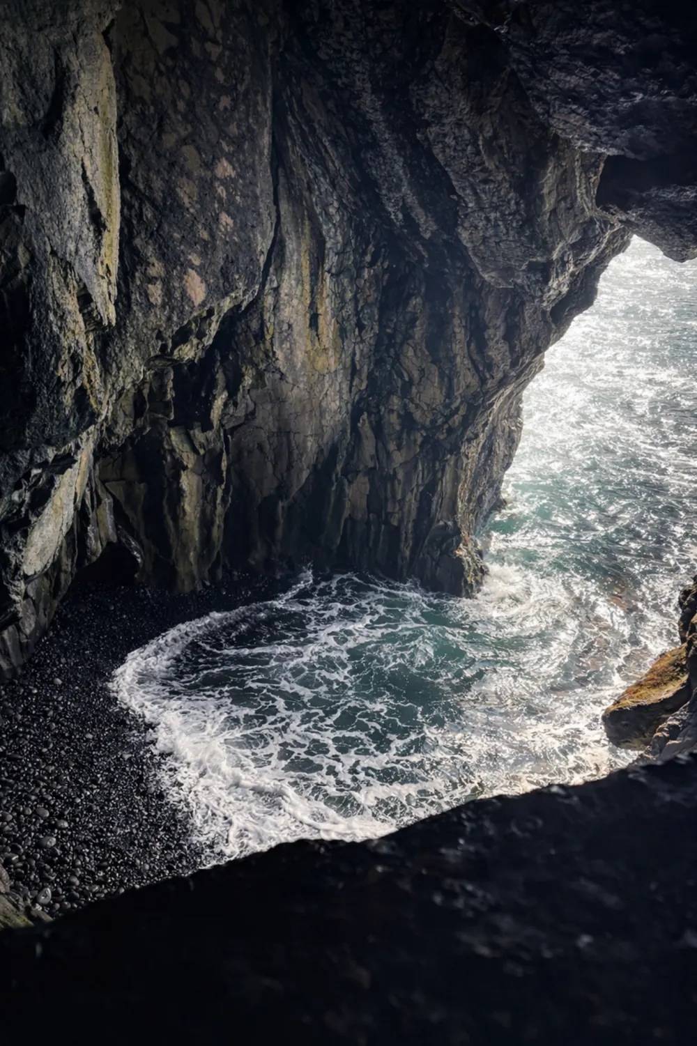 Atlantic waves rolling into a volcanic sea cave with a black pebble beach